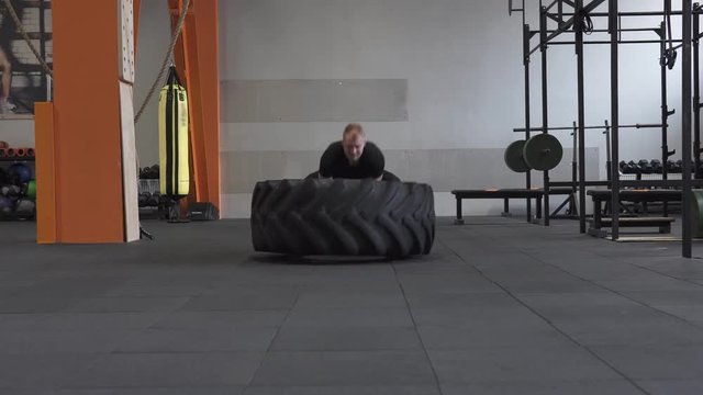 Fitness man doing big tire flips exercise in gym