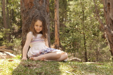 Young girl sitting on grass against tree