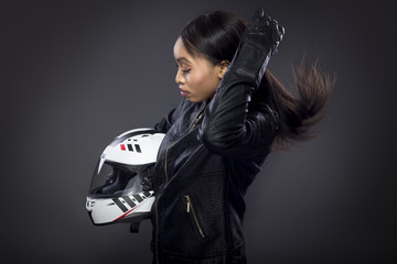 Black female motorcycle rider or race car driver wearing a racing helmet and leather jacket. Part...