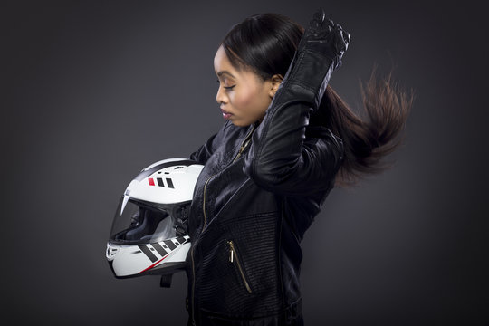 Black female motorcycle rider or race car driver wearing a racing helmet and leather jacket. Part of the gritty woman series, a competitive biker or racer getting ready for competition.