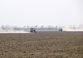 The tractor harrows the soil on the field and creates a cloud of dust behind it