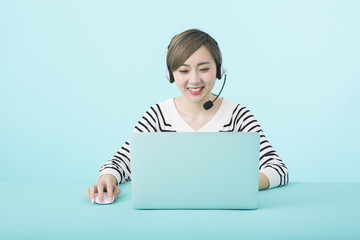 ノートパソコンを操作しながらヘッドセットで話す若い女性