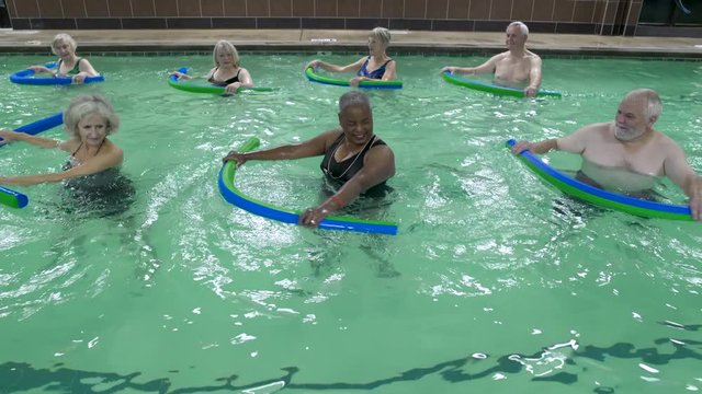 Mature adults exercising with pool noodles in swimming pool.
