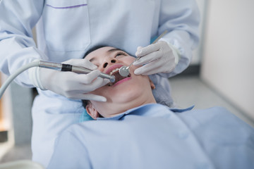 Fototapeta premium Hands of dentist holding a dental tool. Checking the teeth to the woman lying in the dental chair in a hospital.