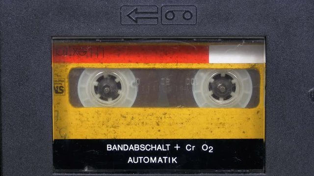 The Vintage Yellow Audio Cassette in the Tape Recorder Rotates. Macro static camera view of a vintage audio cassette tape with a blank label in use sound recording in a cassette player.