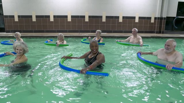 Mature adults exercising with pool noodles in swimming pool.