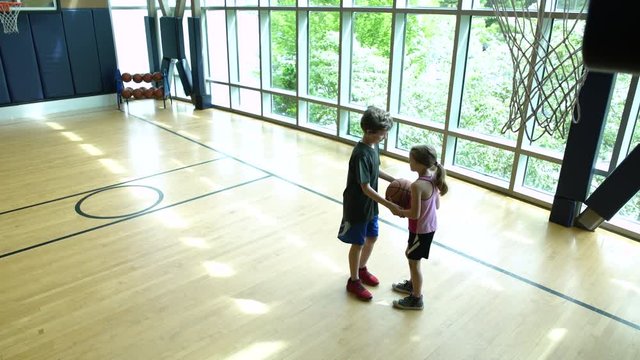 Two children playing basketball in a gym