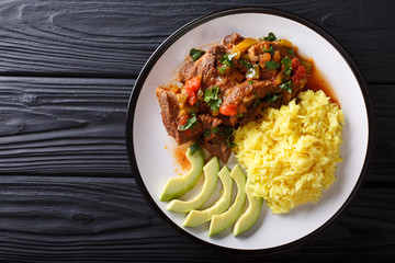 Portion of seco de chivo stewed goat meat with yellow rice and avocado close-up on a plate. Horizontal top view