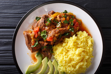 Ecuadorian seco de chivo stewed goat meat with a side dish of yellow rice and avocado close-up on a plate. horizontal top view
