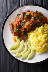 Ecuadorian seco de chivo stewed goat meat with a side dish of yellow rice and avocado close-up on a plate. Vertical top view