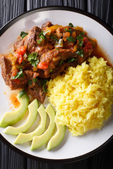 Seco de chivo is goat stew with yellow rice and avocado close-up on a plate. Vertical top view