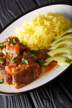 Portion of seco de chivo stewed goat meat with yellow rice and avocado close-up on a plate on the table. vertical