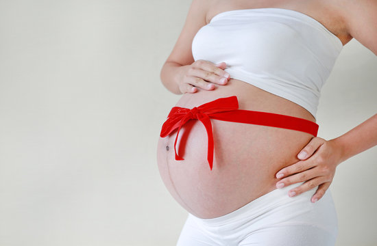 Close-up Pregnant woman's belly with red ribbon.