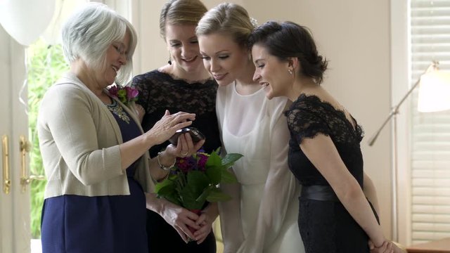 Bride and bridesmaids looking at mother of brides smartphone smiling.