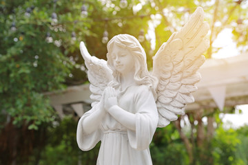Antique statue of a winged angel with praying in the garden with rays of sunlight.