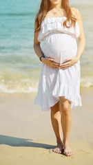 Young beautiful pregnant woman with long hair in white dress on the beach.