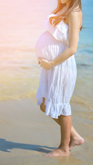 Fototapeta na wymiar Young beautiful pregnant woman with long hair in white dress on the beach.