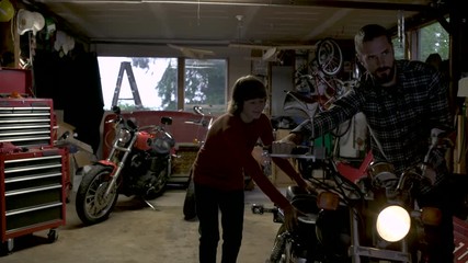 Father and teenage son pushing motorbike in garage.  - Powered by Adobe