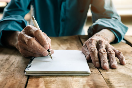 old man writing with a pencil in a notebook,Handwriting on the wood desk
