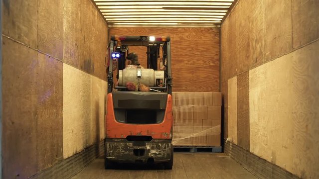 Woman carrying pallet on forklift, reversing from warehouse elevator.