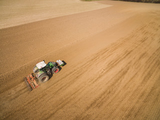 Fototapeta na wymiar aerial view - tractor plows a agricultural field in spring and prepares it for sowing