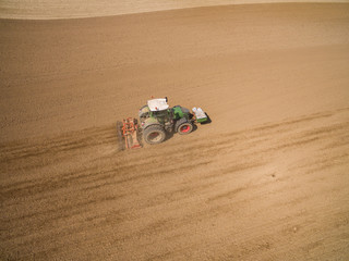 aerial view - tractor plows a agricultural field in spring and prepares it for sowing