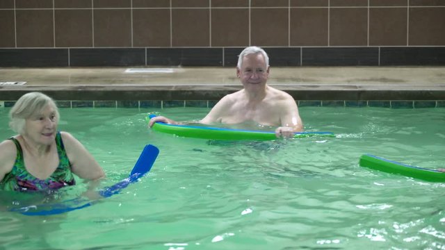 Mature adults exercising with pool noodles in swimming pool.