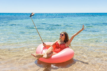 happy Young girl makes selfie in a sprinkled donut float in the sea, smiling with sunglasses for summer