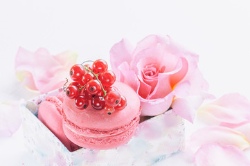Macaroni, red currants, marshmallows against the background of beautiful flowers of roses. Dessert close-up.