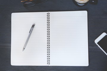 Open the page notepad Office desk table with book, phone, equipment supplies in the work and coffee cup. Top view with copy space on the page paper.