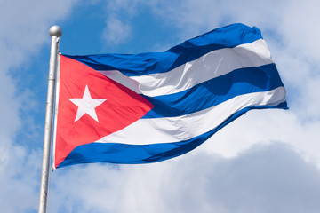 Cuban flag waving in the wind against a blue sky with clouds.