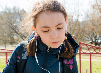 schoolgirl with backpack in warm sunny weather on the street with headphones listening to music in the gadget