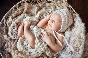 Fototapeta na wymiar Beautiful little newborn boy 20 days sleeps in a basket whith knitted plaid. Portrait of pretty newborn boy