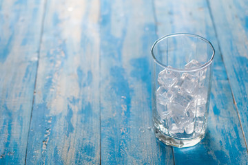 Glass of Ice cube on blue wooden table background.