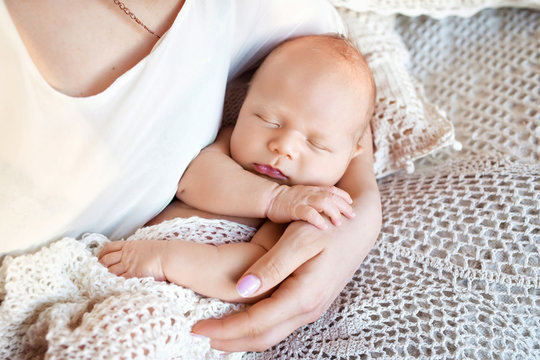 Loving baby sleeping in mother's hands. Closeup picture. Happy mother and her slipping newborn baby in the bed