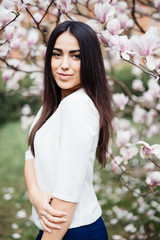 Outdoor portrait of a young beautiful woman near magnolia tree with flowers.