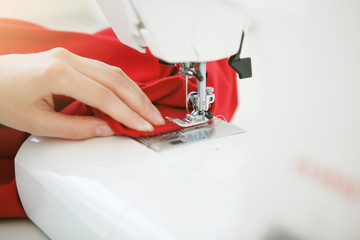 Close up hands of young woman seamstress sitting and sews on sewing machine in studio