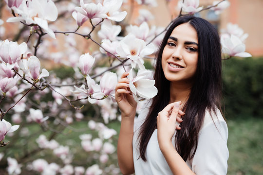 Portrait of a young beautiful lady near magnolia tree with flowers.