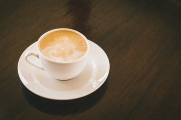 hot cappuccino in white coffee cup on dark wooden desk