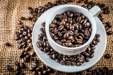 full coffee beans in white coffee cup win burlap background
