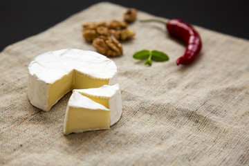 Fototapeta na wymiar White cheese camembert or brie and slices with walnuts and chili pepper. Milk production. Side view.