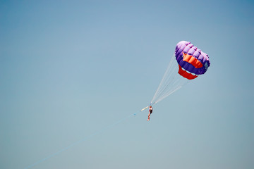 Parasailing. Man flies on parachute in clear blue sky. Side view. Copy space.