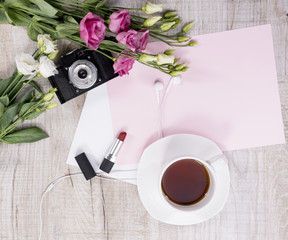 Cup of tea, flowers, vintage camera, earphones, lipstick and sheet of paper