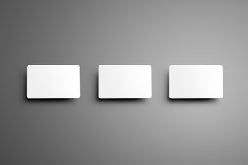 Realistic white mockup of a three  bank (gift) card with shadows placed horizontally on a gray background.