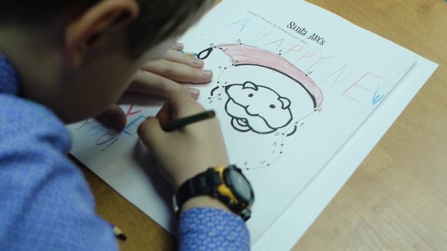 High angle view of boy drawing with color pencil on paper at desk in classroom. Clip. A cute little boy drawing with a pencil close up