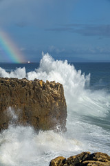 Wild waves breaking over cliff with rainbow
