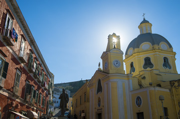 Scenic Mediterranean morning view of the sun rising over a pastel yellow Italian church in the picturesque village of Corricella on the island of Procida