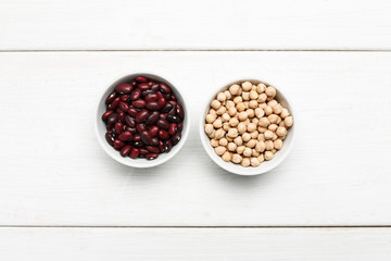 Different beans in bowls on a white wooden table, top view