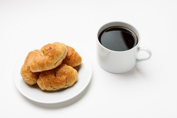 Fresh croissant in a white plate and cup of coffee, top view
