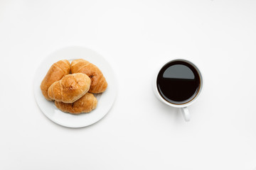 Fresh croissant in a white plate and cup of coffee, top view